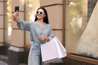 Happy woman with shopping bags taking selfie outdoors