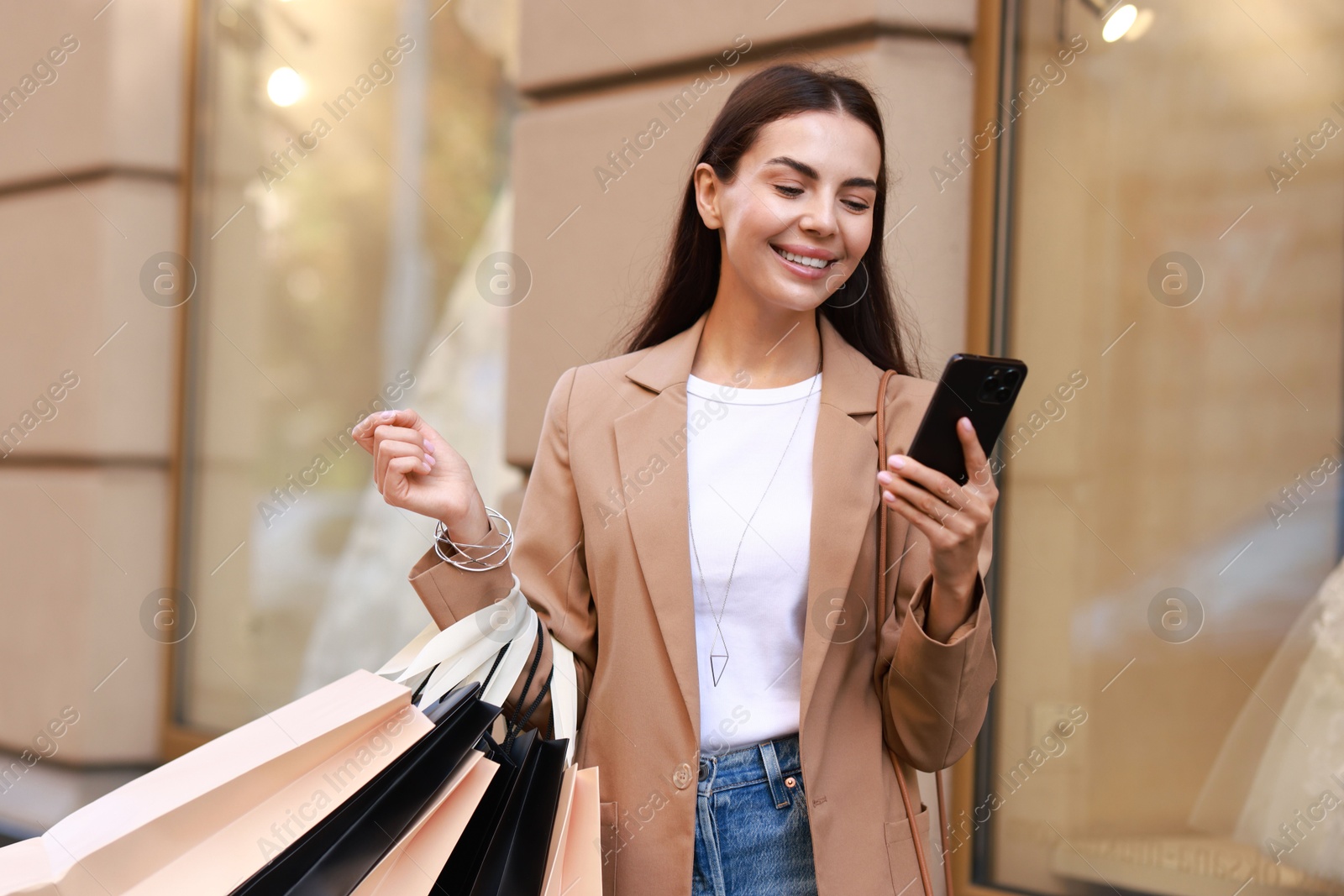 Photo of Happy woman with shopping bags using smartphone outdoors