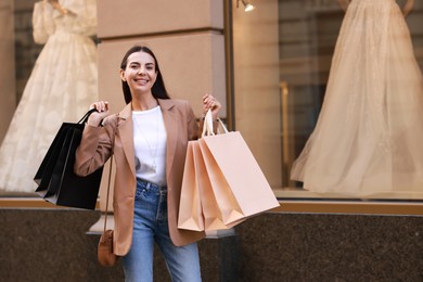 Happy woman with many shopping bags outdoors, space for text