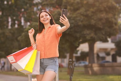 Happy woman with colorful shopping bags taking selfie outdoors, space for text