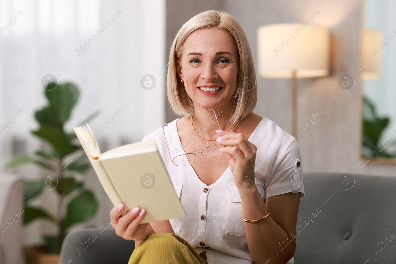 Photo of Portrait of smiling middle aged woman with glasses reading book at home