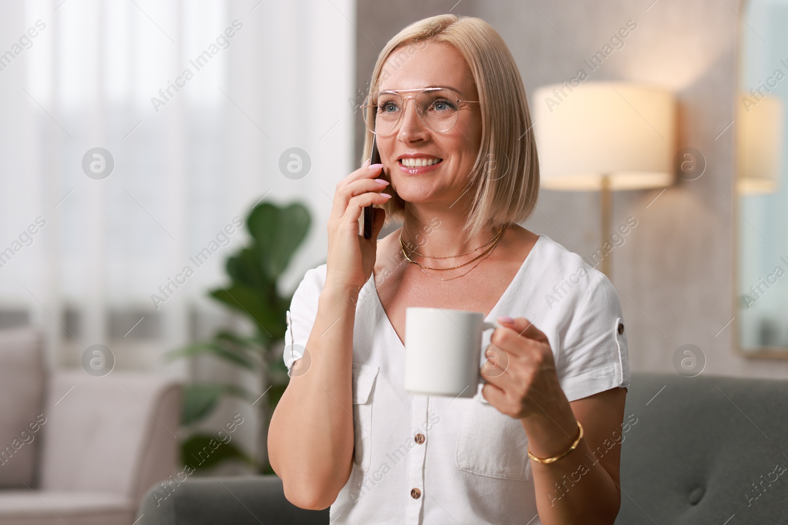 Photo of Portrait of smiling middle aged woman talking by smartphone at home