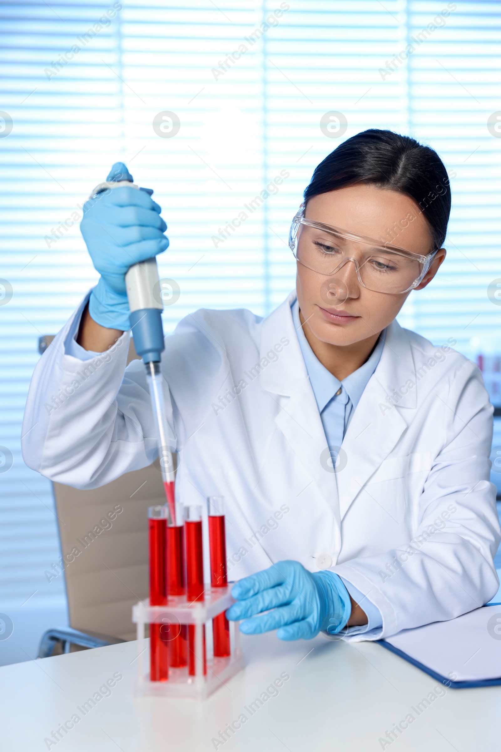 Photo of Laboratory testing. Doctor dripping blood sample into test tube at table indoors