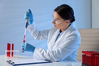 Laboratory testing. Doctor dripping blood sample into test tube at table indoors