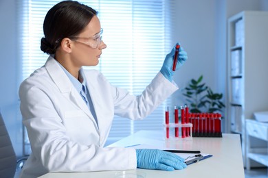 Laboratory testing. Doctor holding test tube with blood sample at table indoors