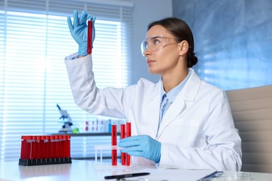 Photo of Laboratory testing. Doctor holding test tube with blood sample at table indoors