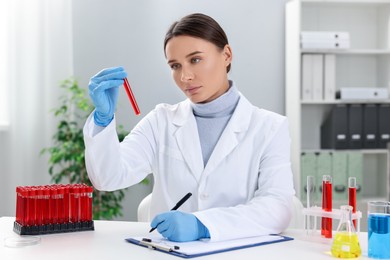 Photo of Laboratory testing. Doctor with blood sample taking notes at table indoors