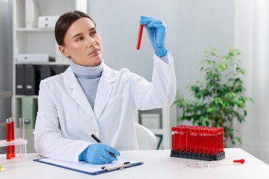 Photo of Laboratory testing. Doctor with blood sample taking notes at table indoors