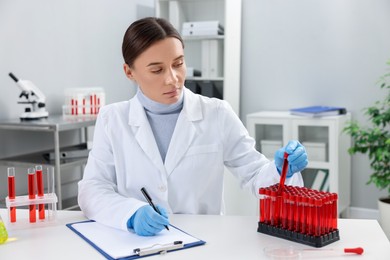 Photo of Laboratory testing. Doctor taking test tube with blood sample while working at table indoors