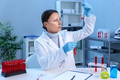 Laboratory testing. Doctor holding test tubes with blood samples at table indoors