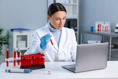 Photo of Laboratory testing. Doctor holding test tube with blood sample at table indoors