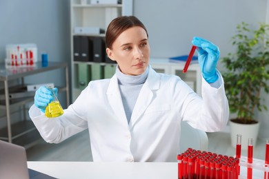 Laboratory testing. Doctor with blood sample in tube and flask at table indoors