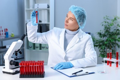 Laboratory testing. Doctor holding test tube with blood sample at table indoors