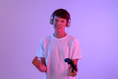 Happy teenage boy in headphones with controller on violet background