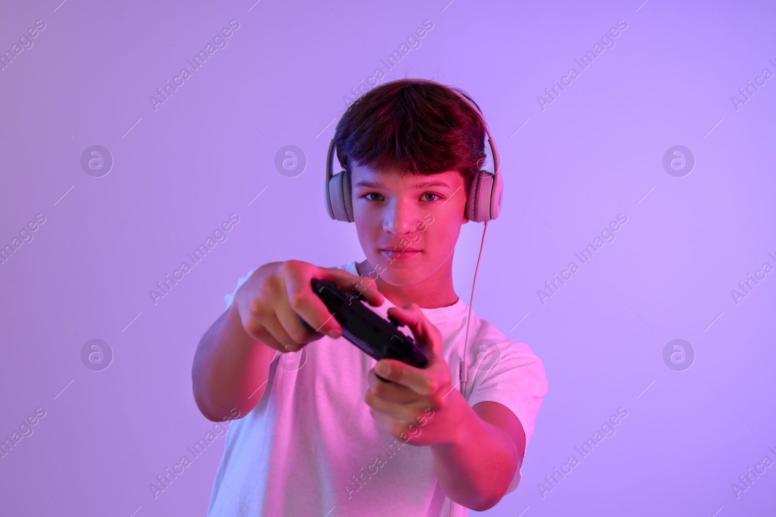 Photo of Teenage boy in headphones playing video game with controller on violet background