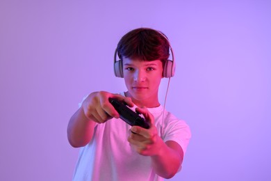 Teenage boy in headphones playing video game with controller on violet background