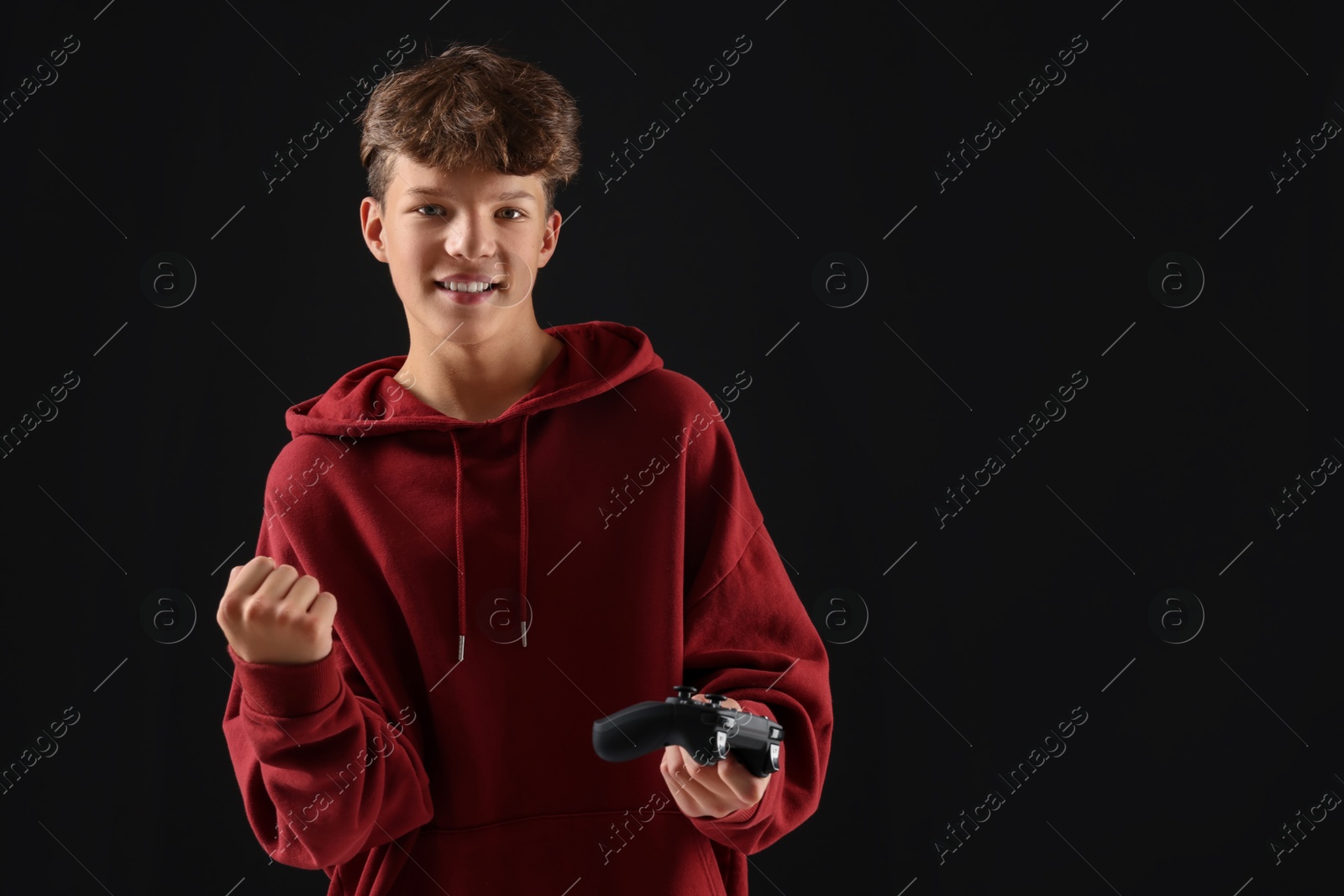 Photo of Happy teenage boy with controller on black background. Space for text