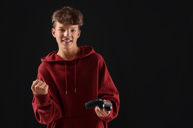 Photo of Happy teenage boy with controller on black background. Space for text