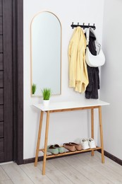 Photo of Mirror, rack with clothes and shoe storage bench in hallway. Interior design