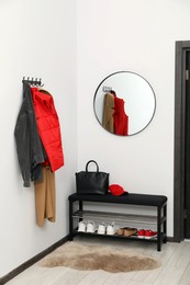 Photo of Mirror, rack with clothes and shoe storage bench in hallway. Interior design