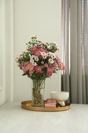 Photo of Beautiful flowers in vase and candles on white wooden table at home