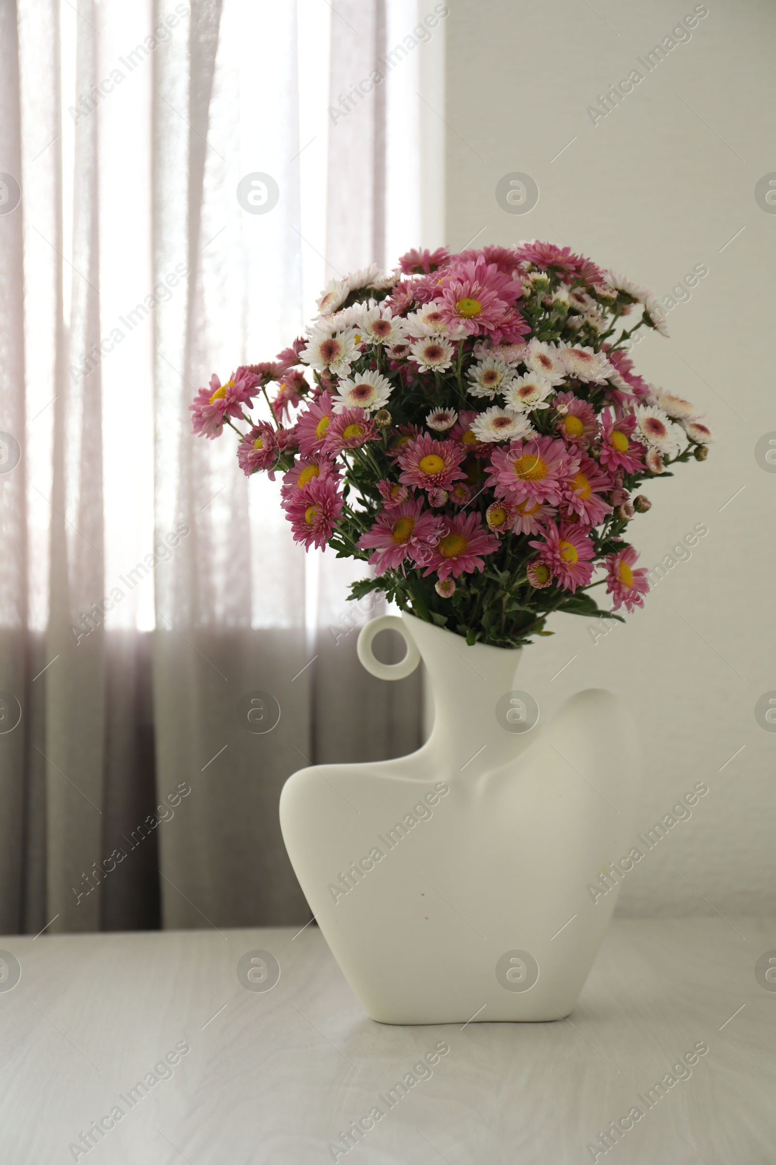 Photo of Stylish vase with beautiful flowers on white wooden table at home