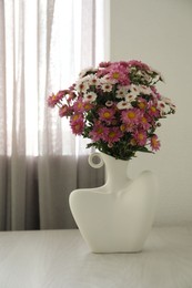 Photo of Stylish vase with beautiful flowers on white wooden table at home