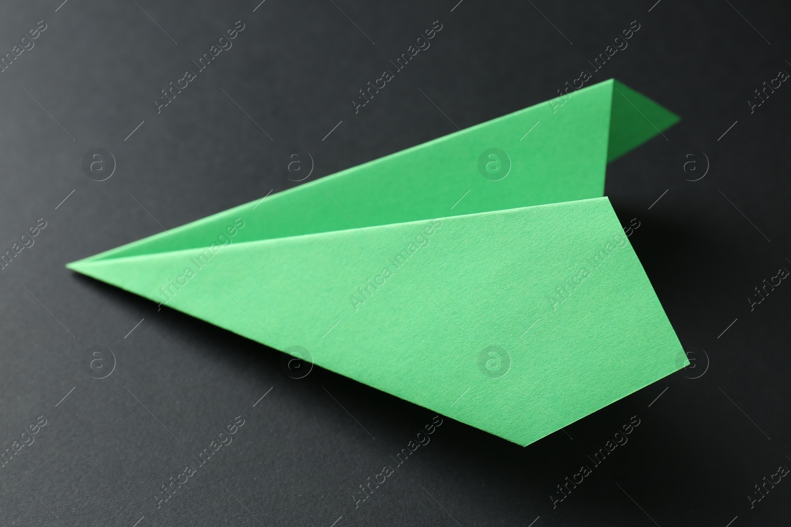 Photo of One handmade green paper plane on black background, closeup