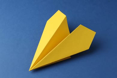 One handmade yellow paper plane on blue background, closeup