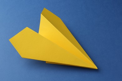 Photo of One handmade yellow paper plane on blue background, closeup