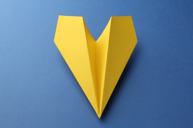 Photo of One handmade yellow paper plane on blue background, closeup