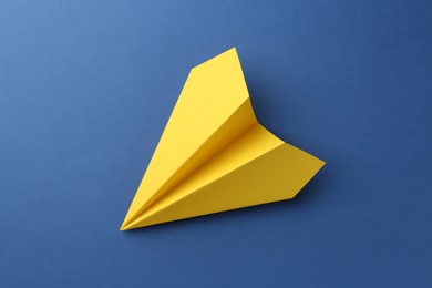 Photo of One handmade yellow paper plane on blue background, top view