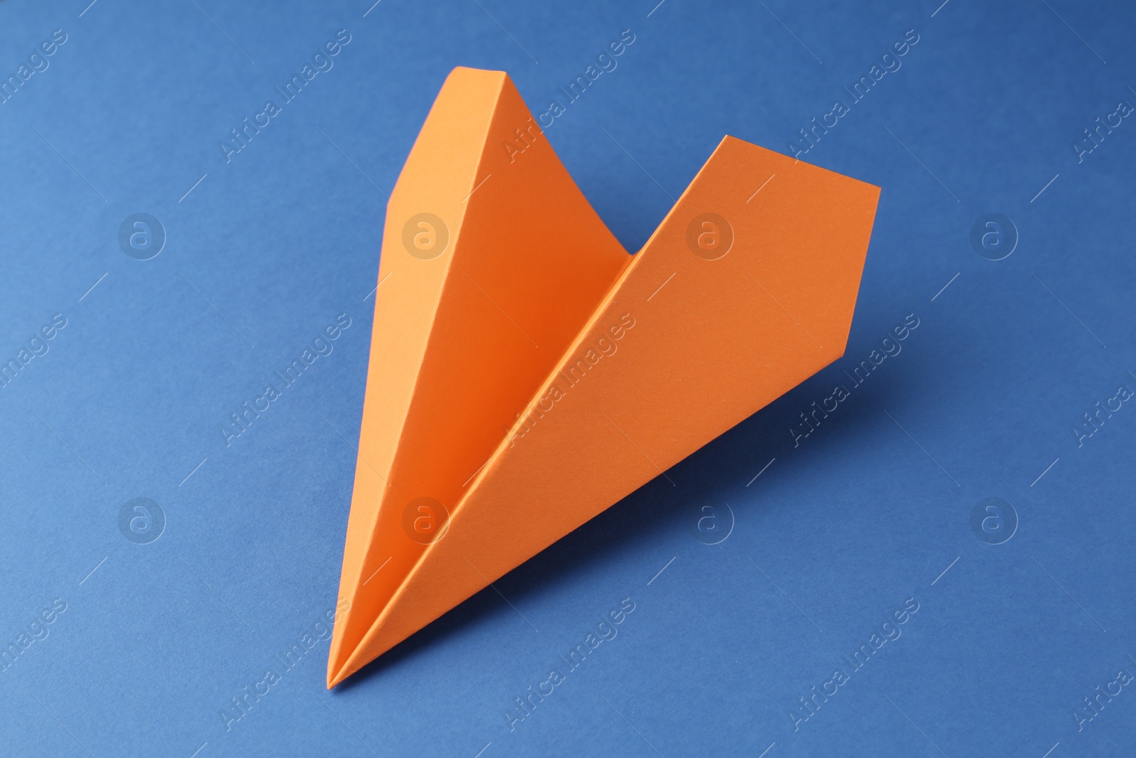 Photo of One handmade orange paper plane on blue background