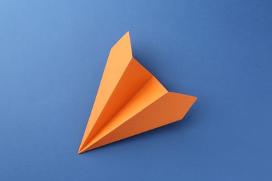 Photo of One handmade orange paper plane on blue background, top view