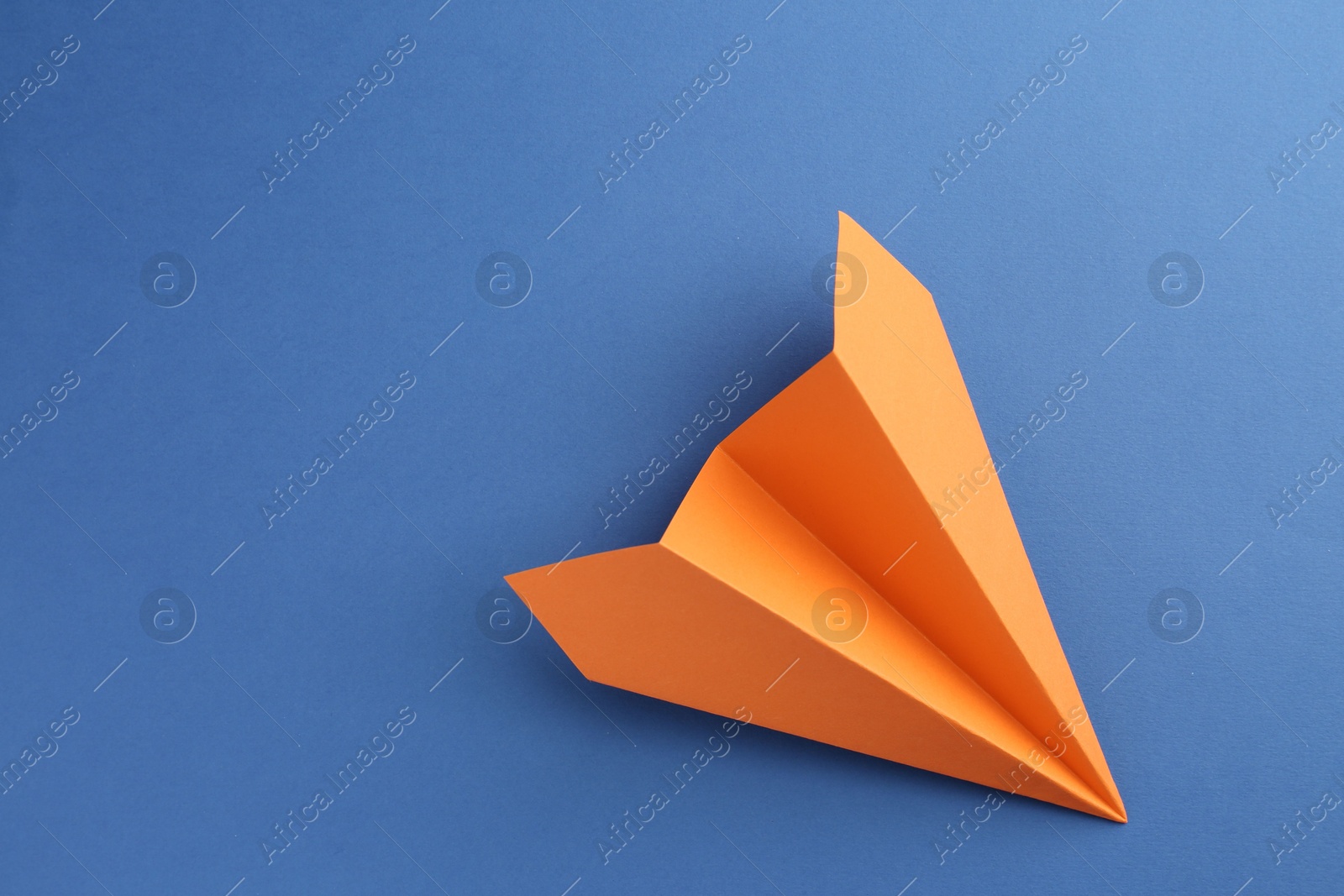 Photo of One handmade orange paper plane on blue background, top view. Space for text