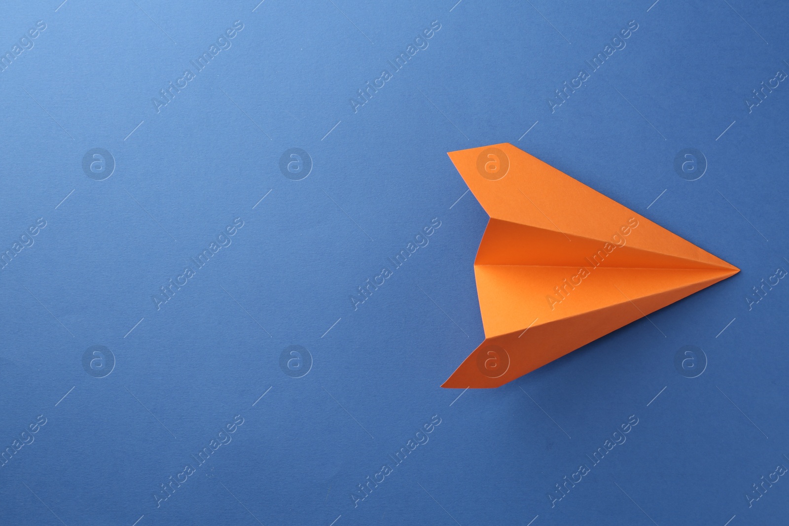 Photo of One handmade orange paper plane on blue background, top view. Space for text