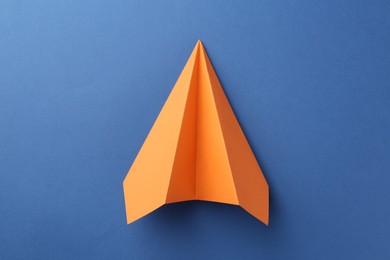 Photo of One handmade orange paper plane on blue background, top view