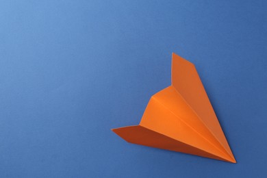 Photo of One handmade orange paper plane on blue background, top view. Space for text