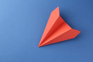 Photo of One handmade coral paper plane on blue background, top view. Space for text