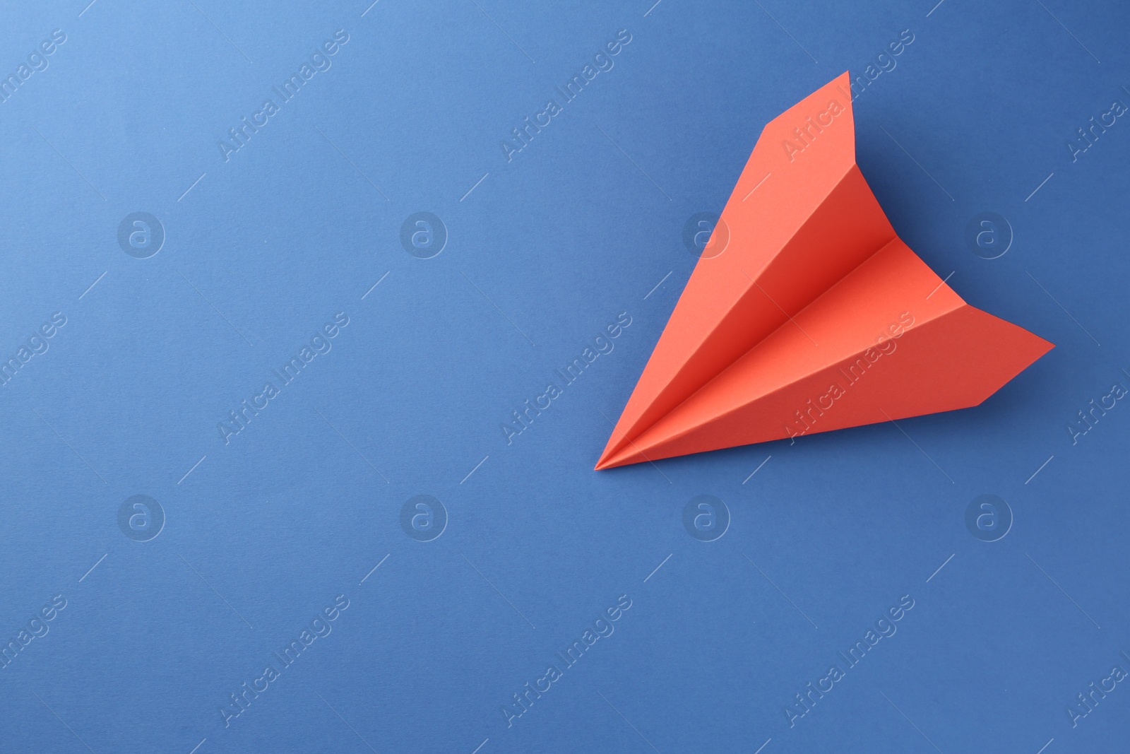 Photo of One handmade coral paper plane on blue background, top view. Space for text