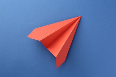 Photo of One handmade coral paper plane on blue background, top view