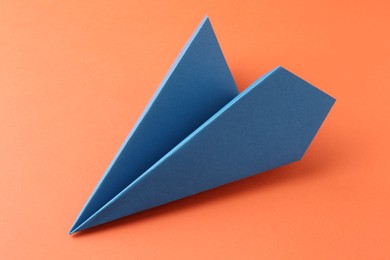 One handmade blue paper plane on orange background, closeup