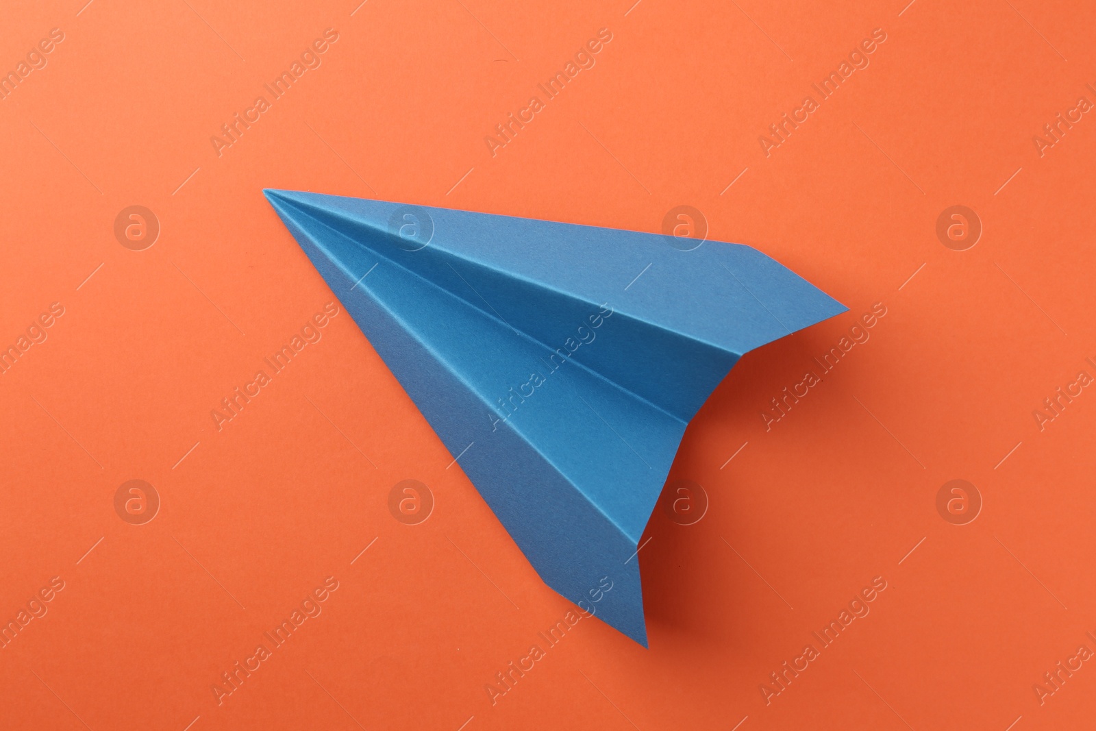 Photo of One handmade blue paper plane on orange background, top view