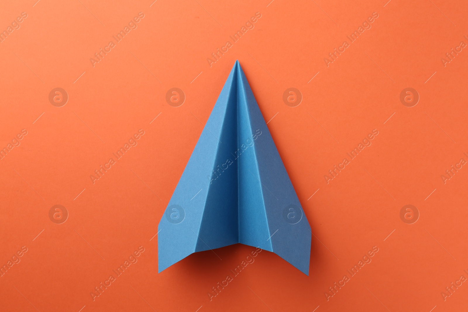 Photo of One handmade blue paper plane on orange background, top view