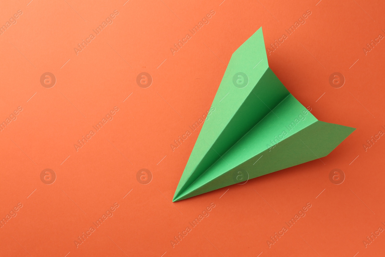 Photo of One handmade green paper plane on orange background, top view. Space for text