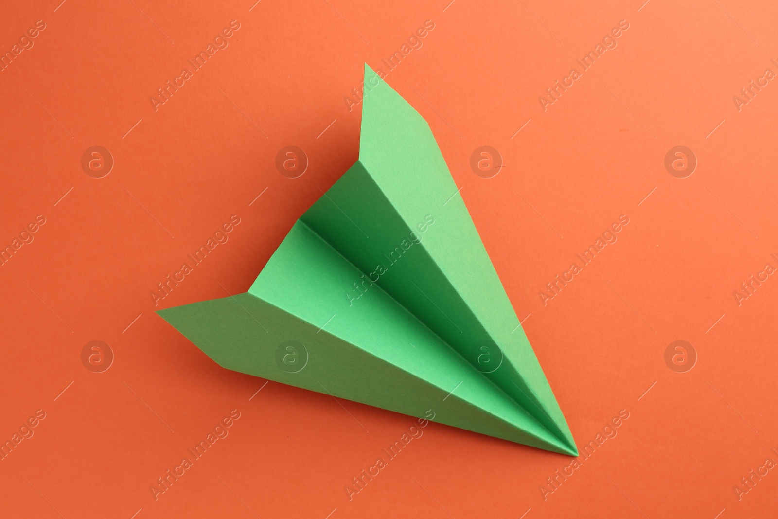 Photo of One handmade green paper plane on orange background, top view