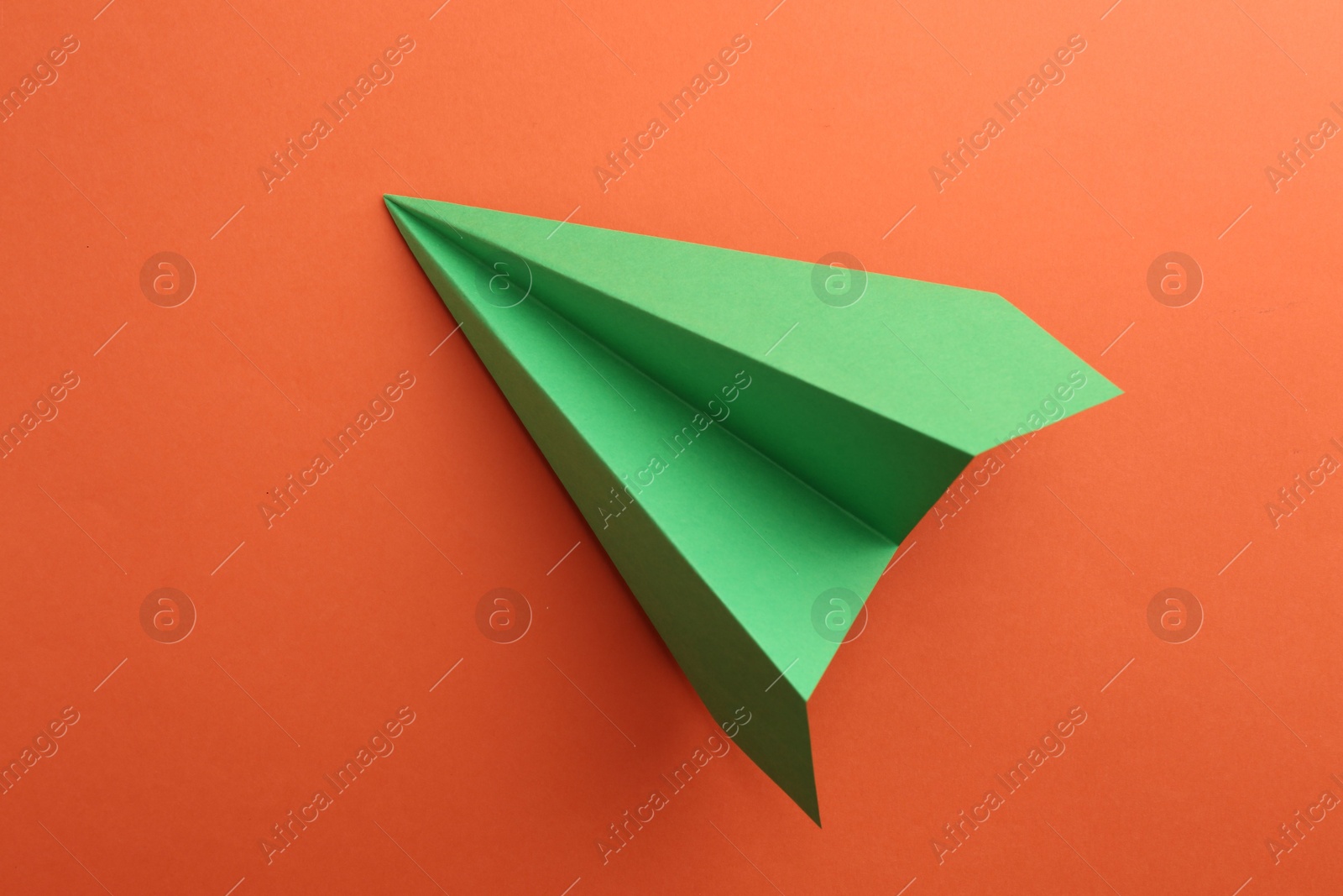 Photo of One handmade green paper plane on orange background, top view