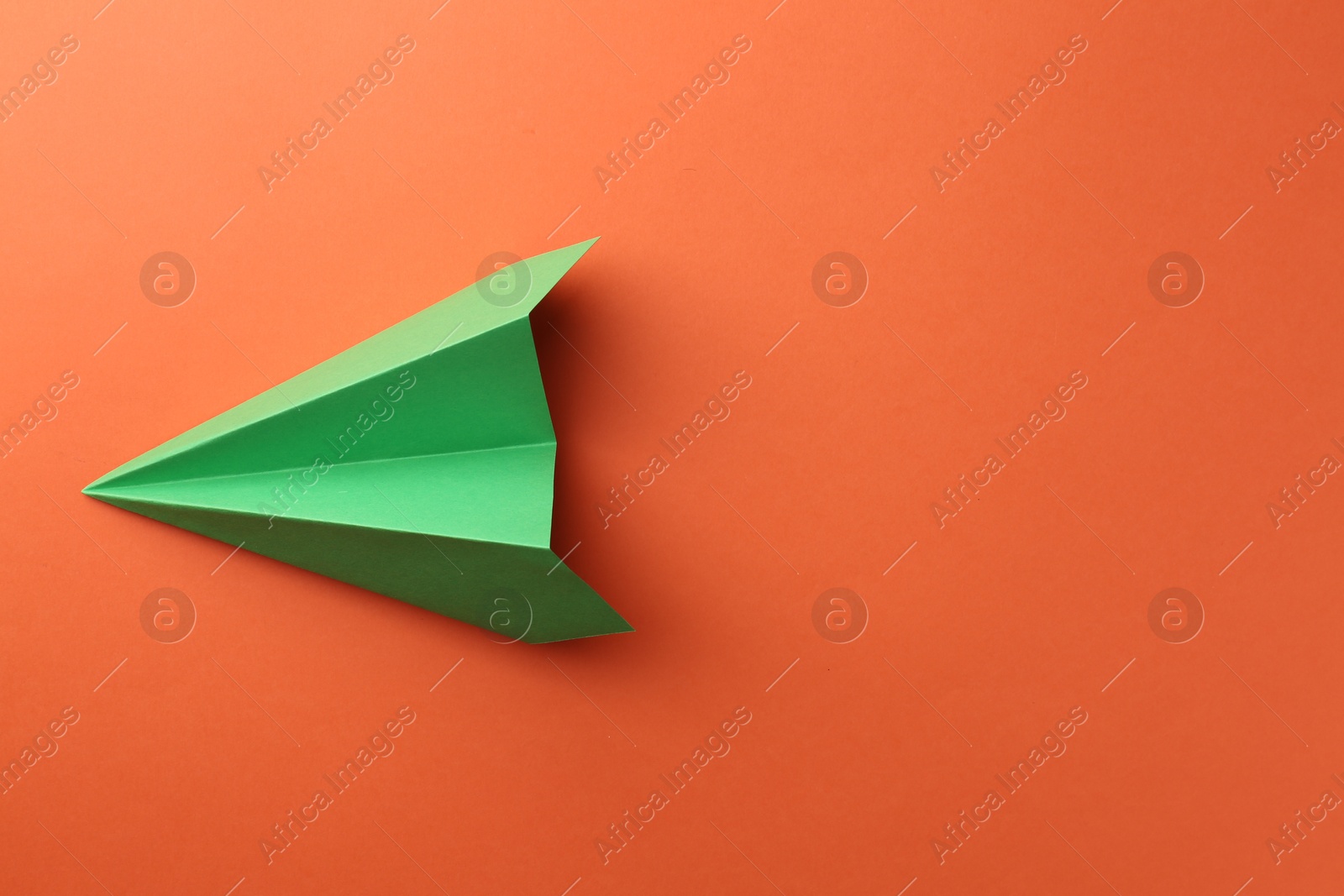 Photo of One handmade green paper plane on orange background, top view. Space for text