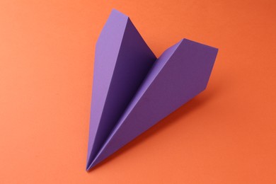 Photo of One handmade violet paper plane on orange background, closeup