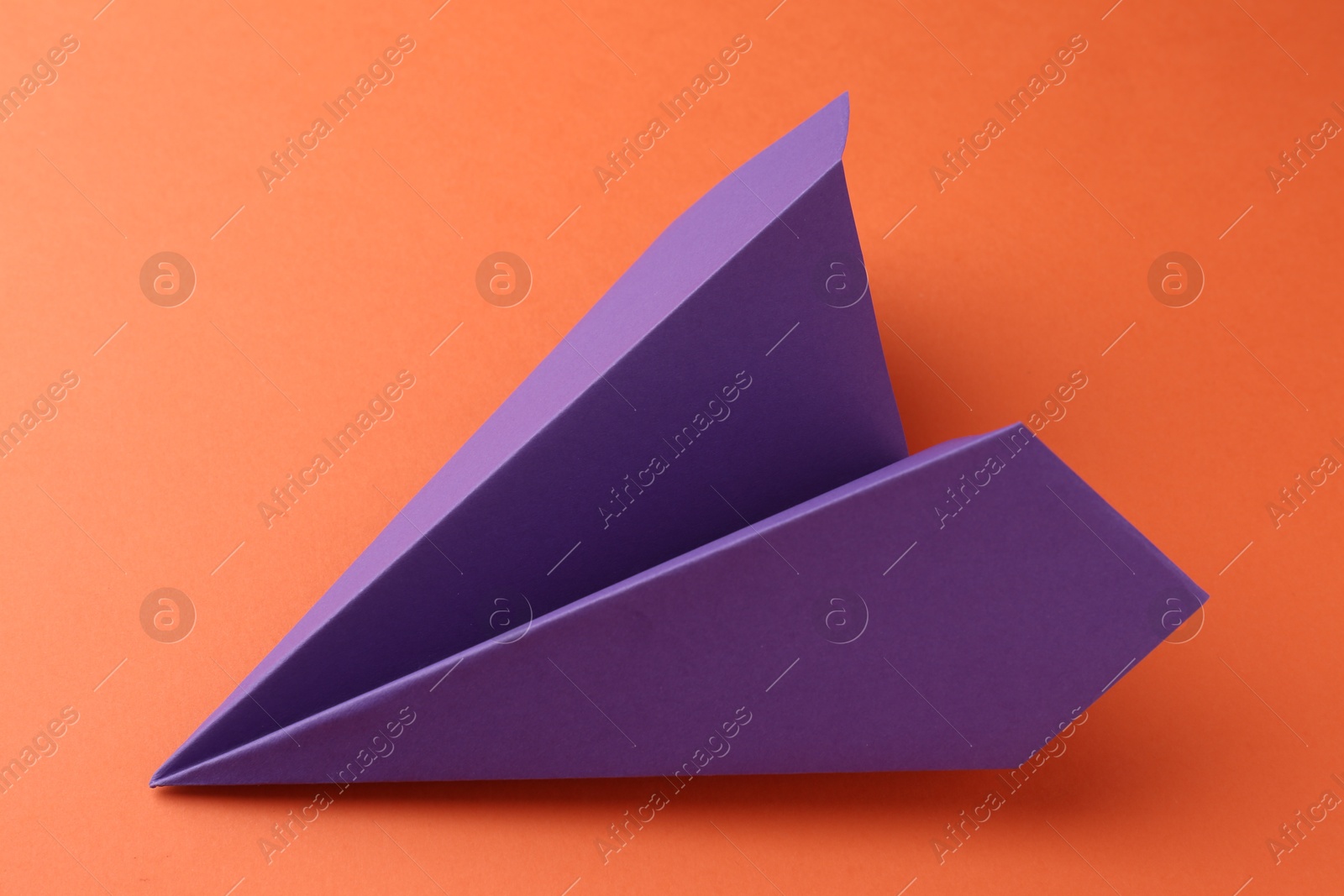 Photo of One handmade violet paper plane on orange background, closeup